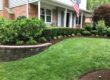 A front yard landscape bed with shrubs, mulch, lawn, and a brick home