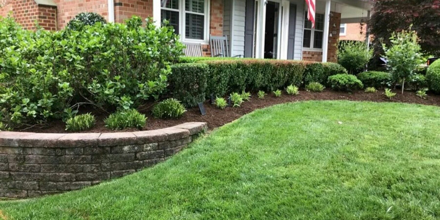 Front yard landscape bed summer prep A front yard landscape bed with shrubs, mulch, lawn, and a brick home